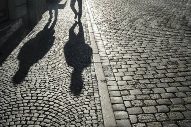Clear shadows of people on a cobblestone pavement. european  pedestrian street in sunset light in summer evening. Black and white. homosexual couple of gays. 