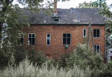 Alman kırmızı tuğlalı evinin dışı. Kahverengi kiremitli çatı. Evin ön cephesi yeşil çimenler ve ağaçlarla çevrili. Kaliningrad bölgesi, Pravdinsk (Friedland), Rusya. Doğu Prusya