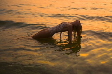 Sarışın, zayıf kadın kumsalda dinleniyor. Kumsalda kumlara uzanmış poz veren, gözleri kapalı seksi sarışın kadın. Yaz fotoğrafı. Güneş batıyor. yoga zen pozu. Omurganın ve sırtın saptırılması