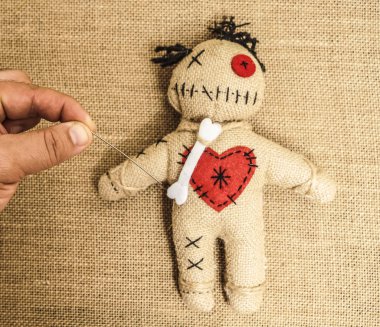 vintage voodoo doll on textile material  background. male hand sticks a doll with a needle