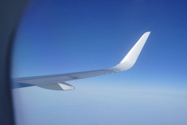 Gökyüzüne bakan uçak penceresi ve uçak kanadı. Mavi gökyüzündeki lombozdan bir yolcu uçağının kanat görüntüsü.