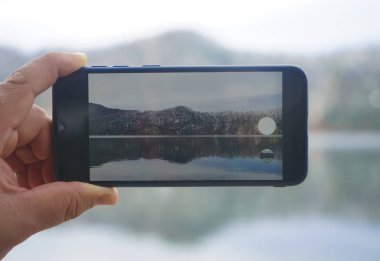Akıllı telefon tutan ve Alpsee 'de fotoğraf çeken adam. Almanya, Bavyera. El ele tutuşup dağ ve gölün fotoğrafını çeken siyah bir akıllı telefon. ekrana odaklan. 