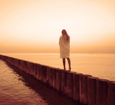 Sarışın güzel bir kadının akşam ya da sabah yürüyüşü. Kafkas sarışın kız gün batımında sahilde yürüyor. Ufuk çizgisine doğrudan giriş yap. Arka, arka manzara. Omuzlarında beyaz ıslak havlu 