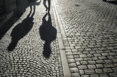 Clear shadows of people on a cobblestone pavement. european  pedestrian street in sunset light in summer evening. Black and white. homosexual couple of gays. 