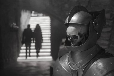 Gri arka planda şövalye miğferi takmış insan kafatası. Çift merdivenleri çıkıyor.