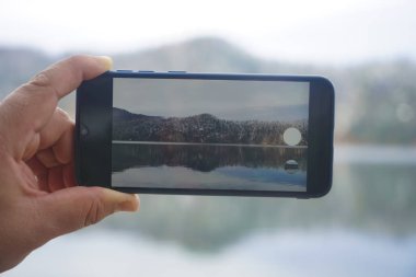 Akıllı telefon tutan ve Alpsee 'de fotoğraf çeken adam. Almanya, Bavyera. El ele tutuşup dağ ve gölün fotoğrafını çeken siyah bir akıllı telefon. ekrana odaklan. 