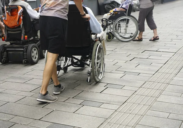 close up view of the feet of a person pushing a wheelchair along a paving stoned street. son behind push wheelchair and his grandfather.