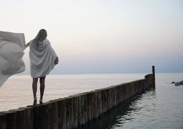 金发美女的晨游 在日落海滩上散步的白人金发姑娘 直达地平线 后视镜 后视镜 白湿巾披在肩上 — 图库照片