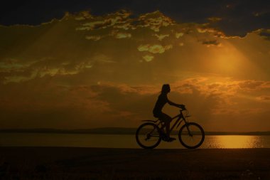 bulutlar ve güneş ışınları ile günbatımı gökyüzüne karşı bisiklet üzerinde sportif turist kadın.