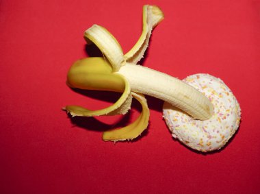  Kırmızı arka planda izole edilmiş donut ve sarı muz. Seks fikri.        