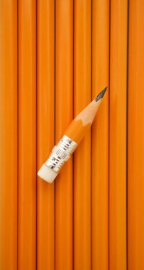 Ters çevrilmiş küçük, keskin bir kalem, sarı kalemlerin üzerinde yükseliyor. Mavi kağıt arkaplanda izole