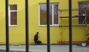 Duvarı sarıya boyuyorum, uzun bir fırçayla. Patenli fırça boyası, çelik yüzey duvarındaki işçilerin koruma ve aşınma için paten fırçasının yanındaki boya. arka görünüm. 