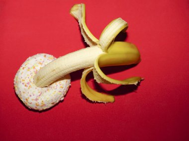  Kırmızı arka planda izole edilmiş donut ve sarı muz. Seks fikri.        