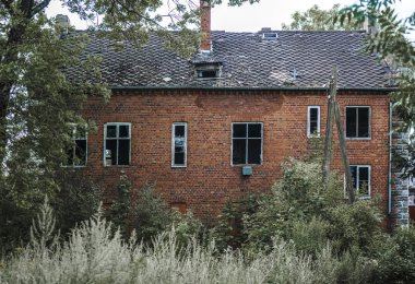 Alman kırmızı tuğlalı evinin dışı. Kahverengi kiremitli çatı. Evin ön cephesi yeşil çimenler ve ağaçlarla çevrili. Kaliningrad bölgesi, Pravdinsk (Friedland), Rusya. Doğu Prusya