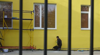 Duvarı sarıya boyuyorum, uzun bir fırçayla. Patenli fırça boyası, çelik yüzey duvarındaki işçilerin koruma ve aşınma için paten fırçasının yanındaki boya. arka görünüm. 