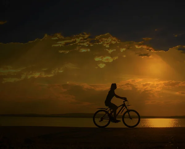 运动的旅游妇女在自行车对日落天空与云和太阳光线 — 图库照片