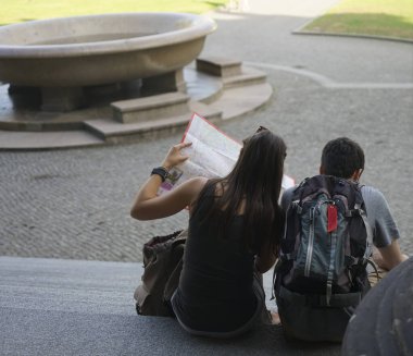 Genç mutlu çift taş merdivenlerde oturuyor ve kağıt haritaya bakıyor. Berlin, Almanya. 