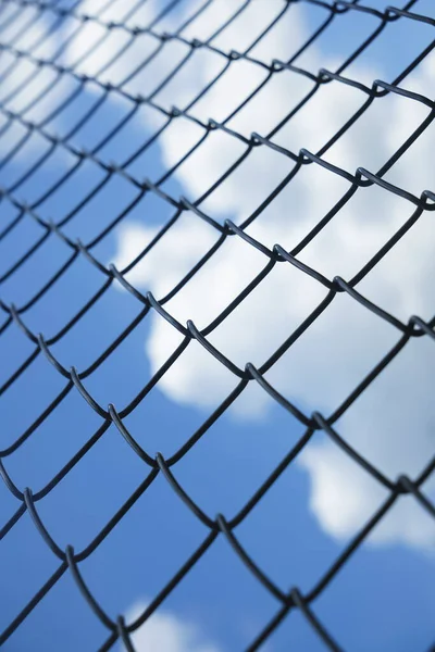 Fence on a blue sky with clouds, Mesh fence with partly cloudy sky, Chain link fence and a blue sky, fence and Blue sky background beyond. Soft focus.