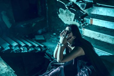 Yüzüne yakın el ele tutuşan soytarı kadın eski bir şatonun bodrumunun derinliklerinde karanlık bir taş merdivenin içinde oturuyor. Kabus, korku konsepti. Dairesel merdiven.