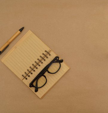 Açık defter, kalem, gözlük ve yeşil bitkiye sahip üst görünüm masası - kahverengi el işi kağıt zemin üzerinde kopya alanı ile saksı