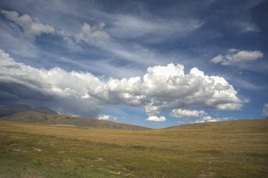 Vadide bir gölü aydınlatan tepeler. Resimde çimenler, kayalar ve dağlar da yer aldı. Yeşil tarlalar, dağlar ve bulutlu gökyüzü günbatımı. Güzel manzara, çimenler. Altai Dağı 