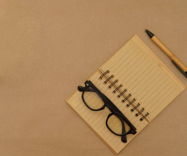 Açık defter, kalem, gözlük ve yeşil bitkiye sahip üst görünüm masası - kahverengi el işi kağıt zemin üzerinde kopya alanı ile saksı