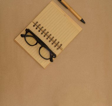 Açık defter, kalem, gözlük ve yeşil bitkiye sahip üst görünüm masası - kahverengi el işi kağıt zemin üzerinde kopya alanı ile saksı