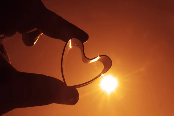 silhouette of one Heart Shape in the Hand on sunrise Sky Background.