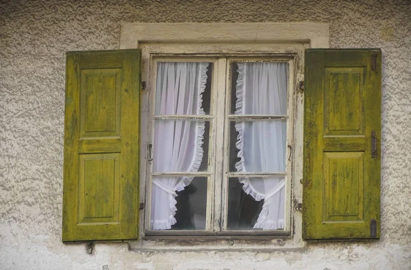 Wooden green window shutters. Window on a white wall with yellow shutters. old window frame with white curtains. Window with shutters in the house close-up. Garmish, Bavaria, Germany.