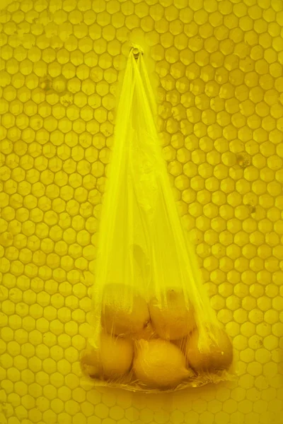 many - five lemons -  food in plastic package recycling and environment eco problem concept. 5 Lemons hanging  in plastic transparent on honeycomb  background