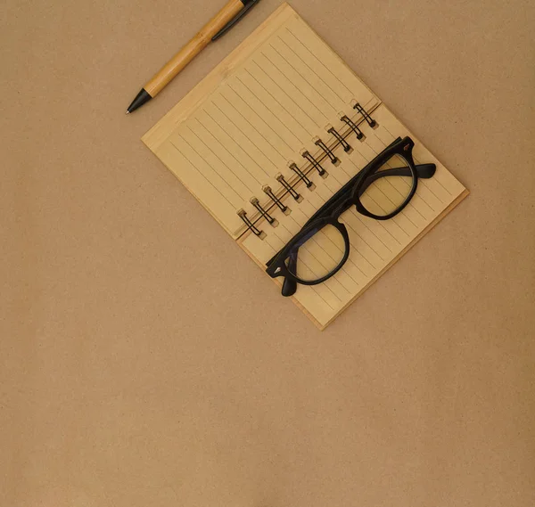 Açık defter, kalem, gözlük ve yeşil bitkiye sahip üst görünüm masası - kahverengi el işi kağıt zemin üzerinde kopya alanı ile saksı