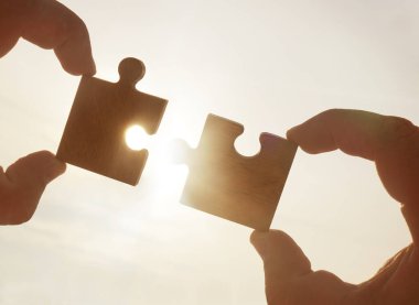 Gökyüzü arka planında yapboz parçaları olan eller.  