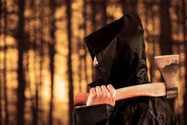 Karanlık, kalın ormanda sisli ve gizemli bir konsepti olan silahlı bir tetikçi. Adam kapüşonlu siyah kefen takıyor. Omzunda balta var. Çam ormanında gün batımı. Yüzü yok. Tanımlanamayan kişi. 