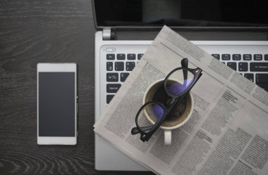 Gazete, cep telefonu, dizüstü bilgisayar, bardak ve bir fincan kahve..