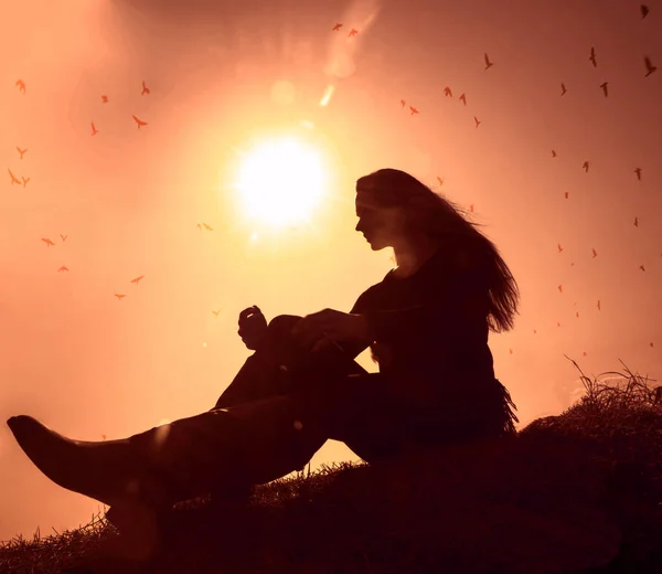 Freedom and feel good concept. Copy space of silhouette woman sitting above hill  on sunset sky  colorful  light and birds fly background.