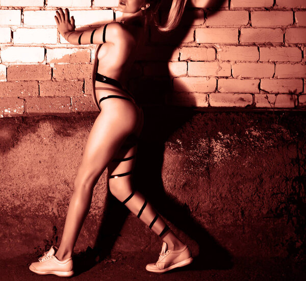 Sexy female semi nude body. young woman posing. Dramatic shadow on brick wall texture