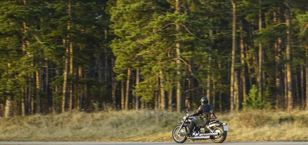 チョッパーバイクの若い男 美しい秋の森と緑の牧草地で空の道路に乗ってバイクに乗る — ストック写真