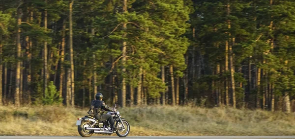チョッパーバイクの若い男 美しい秋の森と緑の牧草地で空の道路に乗ってバイクに乗る — ストック写真