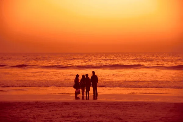 Silhouette of Happy family standing on the beach on the dawn time. Mother, father  and two grown, adults daughters  standing on beach at sunset. back, rear view.