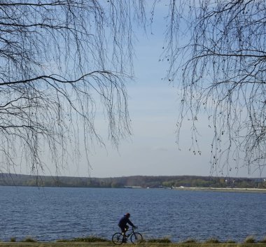 İnsan silueti mavi deniz suyuna karşı açık deniz kenarında bisiklet sürüyor. Mavi gökyüzüne karşı bisikleti olan bir turist hayal edin. Yalnız erkek. Siluet yarışı yüksek hızda 