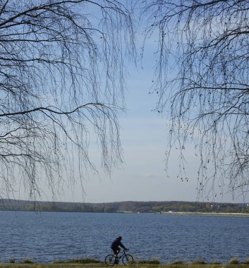 İnsan silueti mavi deniz suyuna karşı açık deniz kenarında bisiklet sürüyor. Mavi gökyüzüne karşı bisikleti olan bir turist hayal edin. Yalnız erkek. Siluet yarışı yüksek hızda 