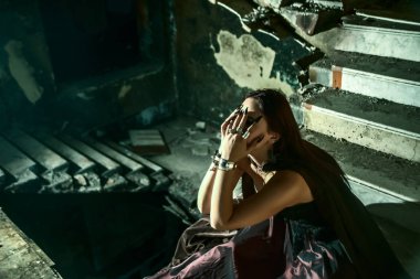 Yüzüne yakın el ele tutuşan soytarı kadın eski bir şatonun bodrumunun derinliklerinde karanlık bir taş merdivenin içinde oturuyor. Kabus, korku konsepti. Dairesel merdiven.