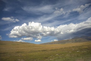Tepeler, vadide bir göl yakmak. Resimde otlar, kayalar ve dağlar da yer aldı..