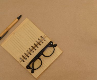Üst görünüm masası açık defter, kalem, kahverengi el işi kağıt zemin üzerinde kopya alanı olan gözlük