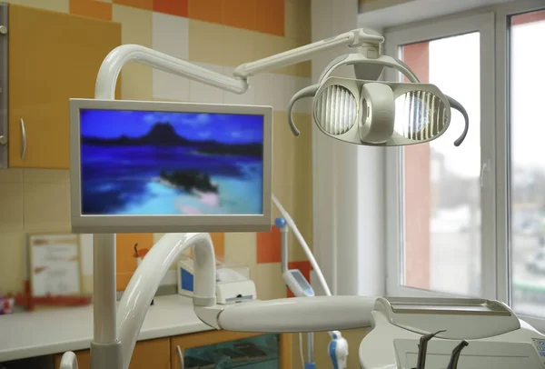 Dental clinic with modern interior design and big window. Dental chair, equipment, tools, computer and other accessories used by dentists. Cabinet in orange and white colors