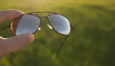 Erkek El, taze yeşil çim ya da çayır ve günbatımı arka planında güneş gözlüğü tutuyor. şık aksesuarlar. 