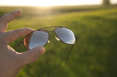 Erkek El, taze yeşil çim ya da çayır ve günbatımı arka planında güneş gözlüğü tutuyor. şık aksesuarlar. 