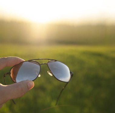 Erkek El, taze yeşil çim ya da çayır ve günbatımı arka planında güneş gözlüğü tutuyor. şık aksesuarlar. 