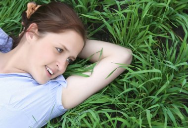 Kafasının altında eli olan mutlu kızıl kız yeşil çimlerin üzerinde yatıyor. en üstteki görünüm. 