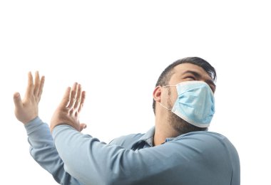 Onu Coronavirus 'tan koruyacak maskeli bir adam. Corona virüsü salgını. Adam yüzüne karşı el ele tutuşuyor. Maskeli genç adam ayakta duruyor. Kapüşonlu, tıbbi maskeli biri. Beyaz arka planda izole edilmiş. korku fikri.